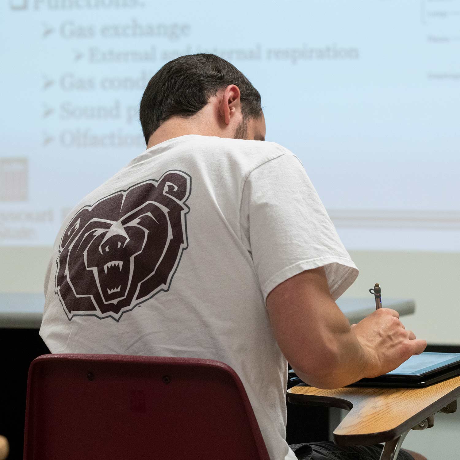 A student writes on a tablet during class.