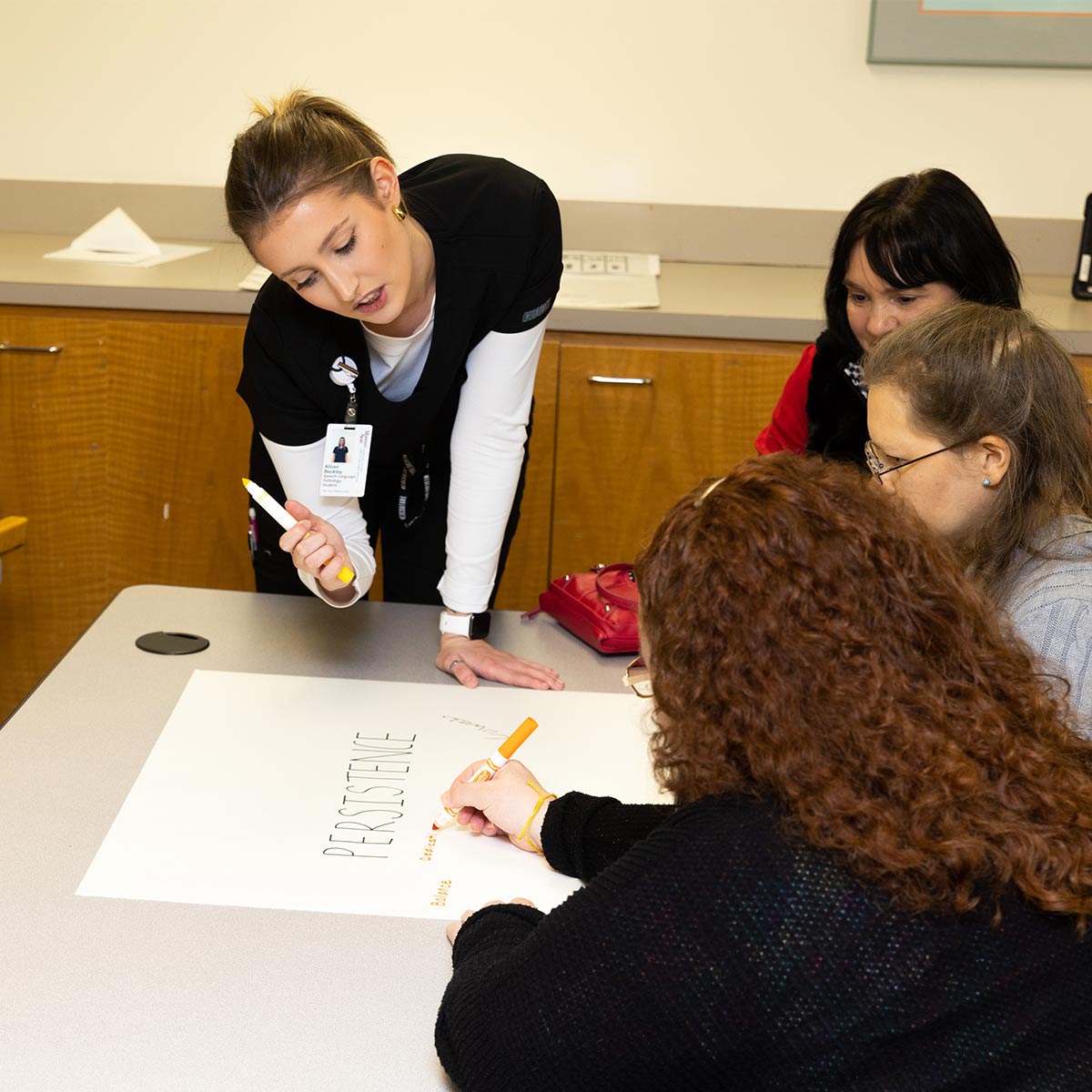 Students and patients do word association by writing on a poster during a speech therapy group class.