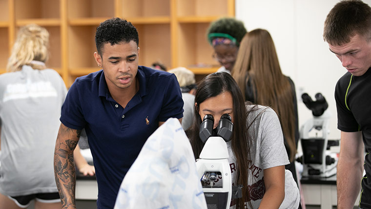 Students looking through microscope in lab. 